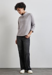 Hellgrauer, strukturierten Pullover mit einem Kragen, Dreiviertelärmeln, kombiniert mit dunklen Jeans und weißen Sneakers. Stehende Pose.