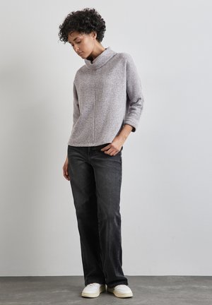 Maglione grigio chiaro, con texture, colletto a cowl, maniche a tre quarti, abbinato a jeans denim scuri e sneakers bianche. Posizione in piedi.