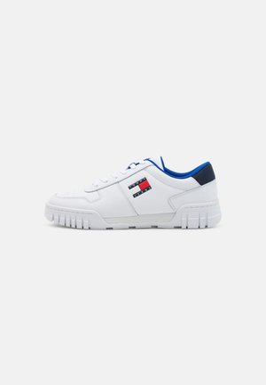 Sneaker bianche con finitura testurizzata, accenti blu e una patch del logo con righe rosse e nere. Presentano una suola spessa e rigata.