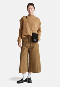 Kárový oversize svetr s žebrovaným výstřihem; široké, khaki odkrojené kalhoty; černá texturovaná kabelka přes rameno se zlatým řetízkovým popruhem; černé polobotky; bílé ponožky.