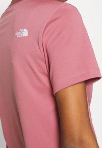 Camiseta de manga corta rosa, hecha de una tela suave, con un logo blanco en la parte posterior, con cuello redondo clásico y costuras cuidadas.