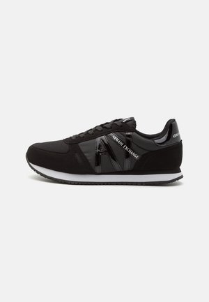 Musta Armani Exchange -lenkkari, jossa on verkko- ja nahkayksityiskohtia, valkoinen pohja, mustat nauhat ja "AX"-logo sivulla. Sivuprofiilinäkyma.