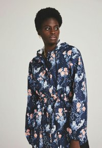 Navy floral jacket made of glossy fabric, featuring pink and blue flower patterns, adjustable hood, and drawstring waist.