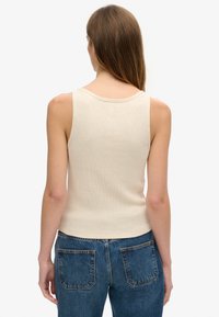 Beige ribbet top med rund halsudskæring, tynde stropper og tætsiddende silhuet, parret med højtaljede blå denimjeans.