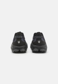 Las zapatillas deportivas negras presentan una parte superior texturizada con acentos morados, un collar acolchado y una suela resistente diseñada para ofrecer tracción.