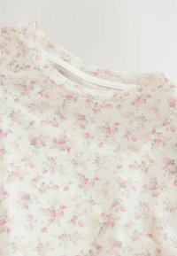 T-shirt en tissu à motif floral présentant de petites fleurs roses et grises sur un fond blanc. Texture douce et encolure ronde.