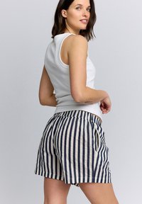 Canotta bianca a coste abbinata a pantaloncini a righe blu navy e crema con tasche laterali e vestibilità comoda. Tessuto liscio e leggero.
