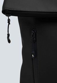 Zaino nero realizzato in tessuto liscio con una tasca con zip, chiusura a coulisse regolabile e dettagli di cucitura sottili.