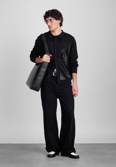 Cárdigan negro con patrón de rayas, pantalones negros y un bolso negro de hombro. Acabados brillantes en el cárdigan y zapatos en contraste.