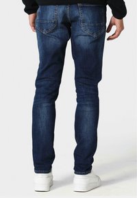 Temno modri kavbojski jeans s slim fit krojem, z dvema zadnjima žepoma in diskretnim zbledelostjo. V kombinaciji z belimi supergami, pogled od zadaj.
