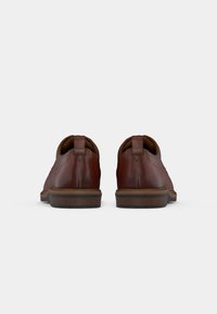 Pair of polished brown leather dress shoes seen from the back with wooden sole and pull tabs against a plain light background.