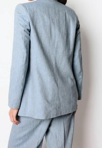 Blazer bleu clair, ajusté, en tissu texturé, avec une coupe droite et des revers classiques. Comprend des épaules structurées et des coutures au dos.