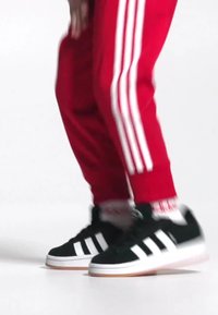 Baskets noires avec des rayures blanches et des semelles en caoutchouc, assorties à des joggers rouges avec des rayures blanches sur les côtés et des poignets texturés.