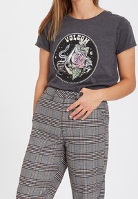 T-shirt gris à manches courtes avec un motif circulaire représentant une rose et une pieuvre. Associé à un pantalon taille haute à carreaux noir, blanc et rouge.