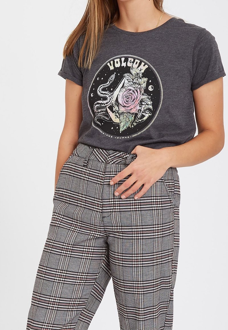 T-shirt gris à manches courtes avec un motif circulaire représentant une rose et une pieuvre. Associé à un pantalon taille haute à carreaux noir, blanc et rouge.