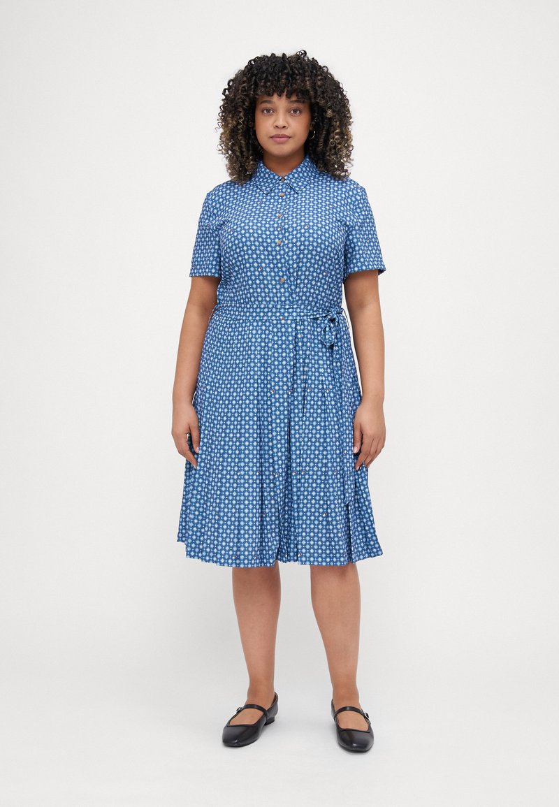 Mėlyna marškinėlių suknelė trumpomis rankovėmis, su gėlių raštu, liemeniu ir plačiu sijonu. Pagaminta iš lengvos medžiagos.