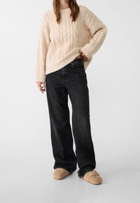 Beige neulottu kaapelikuvioinen villapaita, löysä istuvuus, resorit hihansuissa. Mustat suorat farkut, revityt reunat. Ruskeat pörröiset tohvelit.