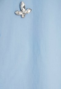 Jasnoniebieska tkanina o gładkiej teksturze, ozdobiona broszką w kształcie kwiatu wykonaną z przezroczystych kamieni szlachetnych.