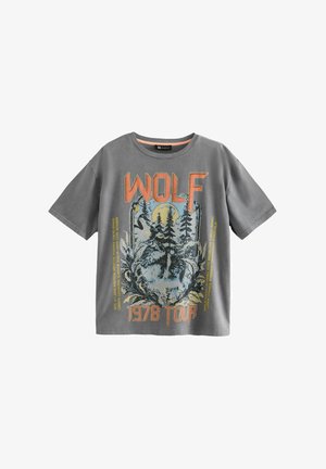 Szürke pamut póló, amelyen egy farkas és fák grafikai nyomata látható, narancssárga és kék szöveggel, amely azt mondja: "WOLF 1978 TOUR". Rövid ujjak.