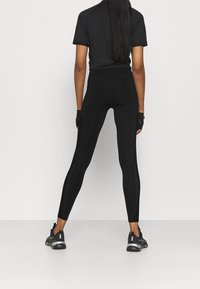 Leggings neri con un design aderente, dotati di pannelli laterali in rete per la ventilazione, abbinati a una maglietta nera a maniche corte e sneakers nere.