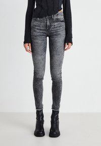 Jeans skinny de tiro alto negros con un lavado gris deslavado, costuras en contraste y dobladillos deshilachados, combinados con elegantes botas negras hasta el tobillo.
