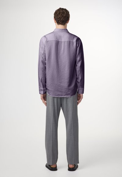 Paarse textuur shirt met lange mouwen, achterste schouderstuk en knoopmanchetten, gecombineerd met lichtgrijze broek met streepjes en zwarte sandaal.