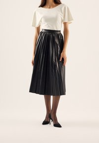 Czarna plisowana spódnica o błyszczącej teksturze, zestawiona z dopasowaną białą bluzką. Całość uzupełniają czarne buty na wysokim obcasie.