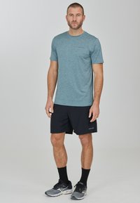 Himmelblaues Kurzarmhemd aus Heather-Stoff, kombiniert mit schwarzen Sportshorts und schwarzen Crew-Socken. Das Hemd hat ein Logo und besteht aus strukturiertem Material.