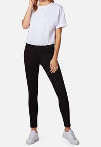 Jeans skinny negros con una cintura de altura media, combinados con una camiseta de algodón blanca con las mangas enrolladas y zapatillas blancas. Textura suave.