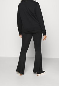 Felpa nera e pantaloni neri a campana, entrambi realizzati in un tessuto morbido. L'outfit presenta un design semplice con polsini e vita a coste.