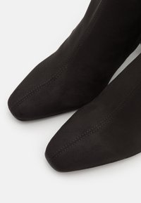 Bottines en cuir suédé noir avec un bout pointu, présentant des détails de couture simples et un design épuré et élégant.