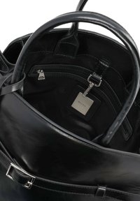 Melnas ādas rokassoma ar gludu tekstūru, apaļu formu un divām rokturiem. Iekšpusē ir rāvējslēdzēja kabata un zīmola birka.