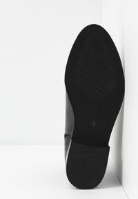Chaussure noire présentant une tige en cuir lisse avec une semelle en caoutchouc texturée, affichant des marquages de taille en dessous.