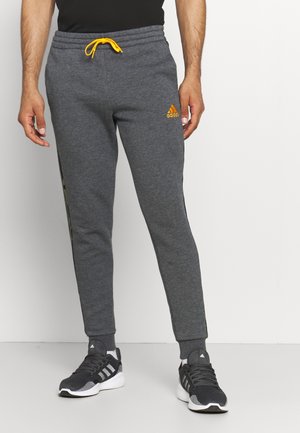 Graue Jogginghose mit orangefarbener Kordel, schmaler Passform, geripptem Bund und Adidas-Logo auf dem linken Oberschenkel; seitliches Musterdetail sichtbar.