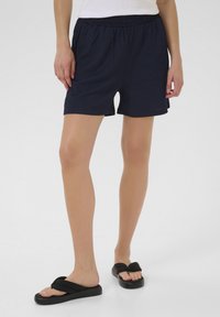 Shorts bleu marine avec une ceinture élastique, texture douce et finition lisse, associés à des sandales flip-flop noires avec un large design de lanière.
