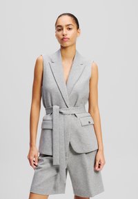 Grijs mouwloos blazer met een diepe V-hals, een ceintuur in de taille en voorzakken; op maat gemaakt ontwerp; zachte stof; gecombineerd met bijpassende shorts.