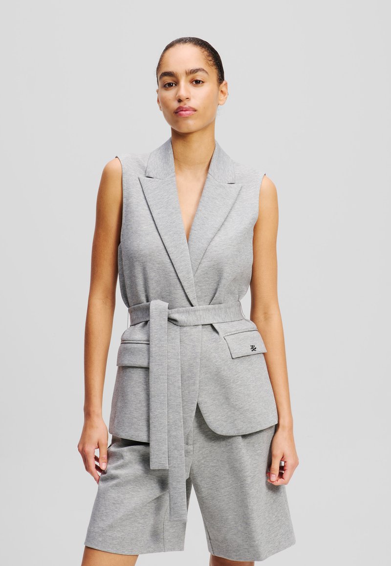 Grijs mouwloos blazer met een diepe V-hals, een ceintuur in de taille en voorzakken; op maat gemaakt ontwerp; zachte stof; gecombineerd met bijpassende shorts.