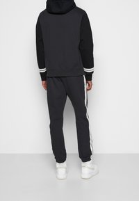 Svart hoodie med en grå baksida, vita randiga detaljer på ärmarna, i kombination med matchande svarta joggers med vita sidostripes och cuffs.