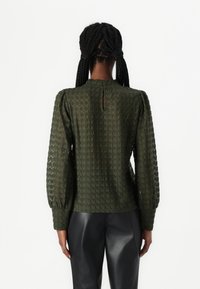 Alyvinės spalvos nėrinių palaidinė su pūstomis rankovėmis, dalinė iškirptė nugaroje, tekstūrinis raštas ir laisvas kirpimas. Suderinta su juodomis odinėmis kelnėmis.