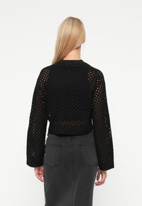 Pull noir en tricot avec un motif de crochet lâche, des poignets côtelés et une coupe courte, associé à une jupe crayon gris foncé.