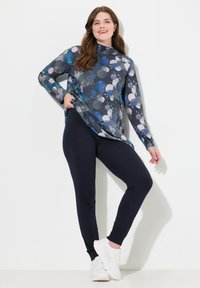 Długi rękaw z wielokolorowym okrągłym wzorem na ciemnym tle, w połączeniu z dopasowanymi granatowymi legginsami i białymi trampkami.