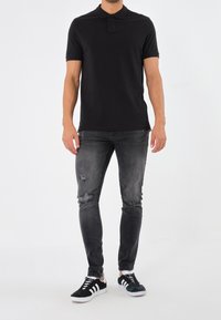 Polo noir avec un col, associé à un jean skinny déchiré gris foncé et des baskets noir et blanc. Design simple et décontracté.