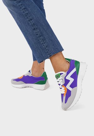 Zapatillas deportivas moradas y grises con acentos en verde y naranja, que cuentan con una suela texturizada y un diseño en zigzag en el lateral.