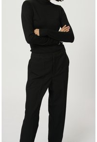 Pull à col roulé noir en tissu tricoté lisse, assorti à un pantalon noir ajusté avec une jambe droite, des plis avant et des poches latérales.
