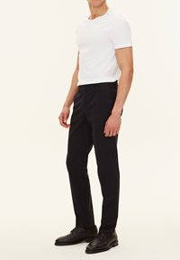 T-shirt bianca in cotone slim fit da uomo abbinata a pantaloni blu scuro e scarpe stringate in pelle nere. Design semplice con una palette di colori neutri.