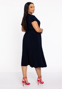 Marineblaues Midikleid mit fließenden Ärmeln, elastischem Bund und gestuftem Rock. Kombiniert mit knallpinken High-Heels.