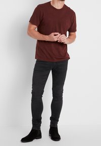 Hnědý bavlněný tričko s krátkým rukávem v kombinaci s černými slim jeansy s žebrovanými detaily na kolenou a černými semišovými kotníkovými botami.