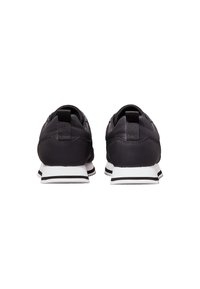 Zapatillas deportivas negras con un diseño elegante, que presentan una parte superior texturizada, suela blanca y acentos en blanco y negro contrastantes.