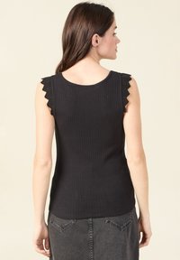 Svart ribbad linne med vågkant vid axlarna, med en figurnära design och rund halsringning. Bakifrån vy visas.