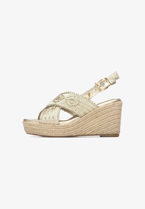 Gouden sleehak sandaal met gevlochten jute hak en gekruiste, textuurbanden. Verstelbare enkelriem met gesp, open teen ontwerp.